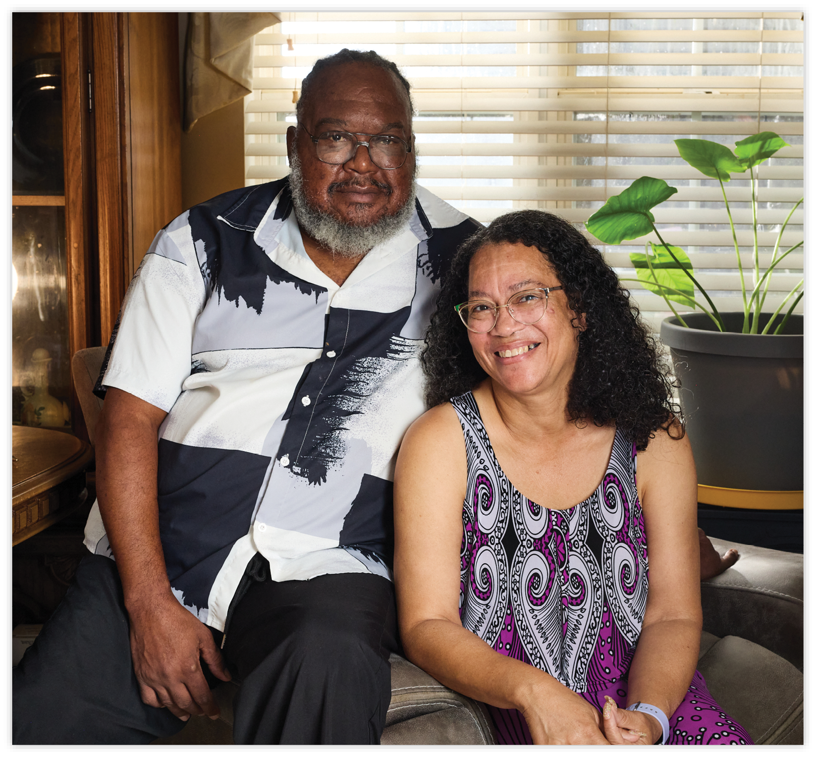 Photograph of Craig and Judy Nicholson sitting on a couch with plants behind them.