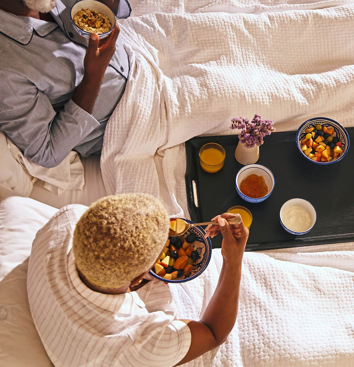 Overhead image of a couple eating breakfast in bed at a hotel.
