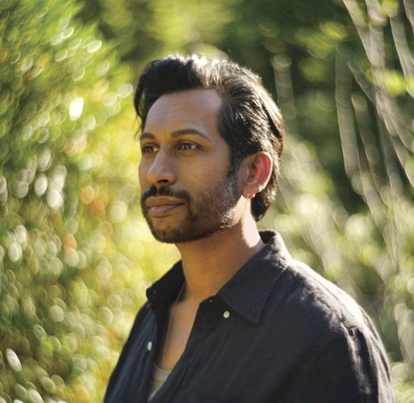 Image of a man looking off to the side surrounded by greenery 