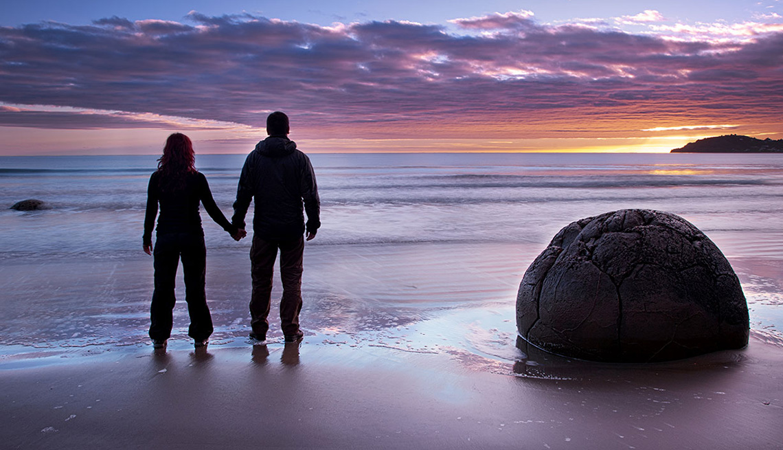 Couple Holds Hands On Beach Looking At Sunset In New Zealand, Best Honeymoon Destinations