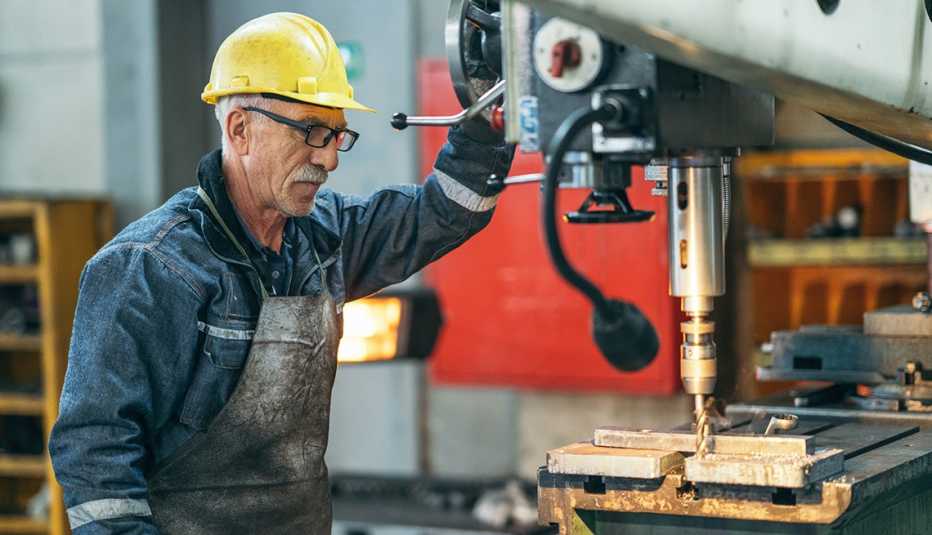 An older worker is standing by a machine