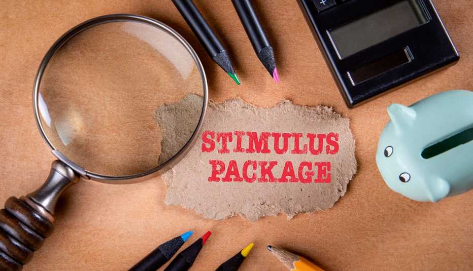 stimulus package note surrounded by magnifying glass, piggy bank, pencils and calculator on a table