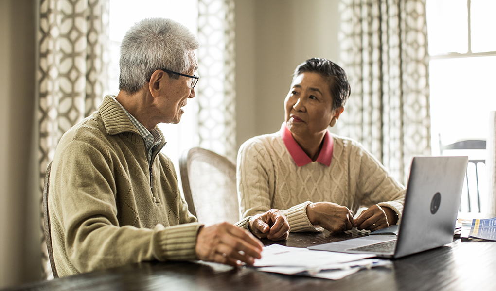 Couple sitting at the table with a laptop looking through their health care directives papers