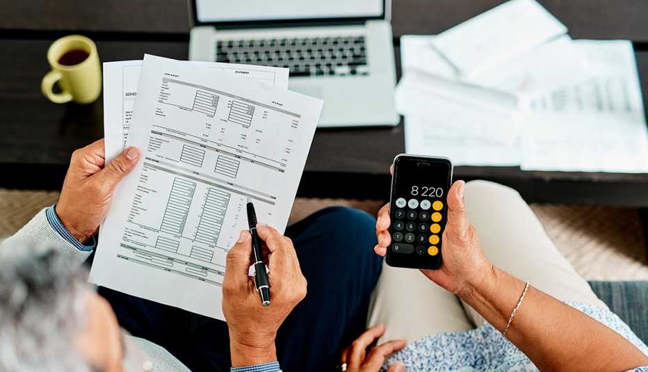 A top view of a couple doing their taxes. One person holds paperwork and one holds a calculator