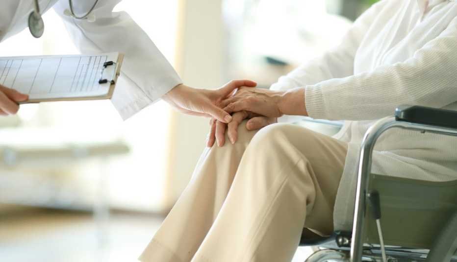a doctor puts their hand over the hands of a patient in a wheelchair