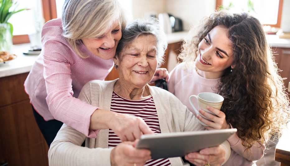 A woman with her mother, who is in a wheelchair and her teenage daughter. All are looking at a tablet together