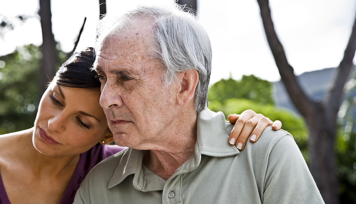 Woman with her arm around her father, both looking sad