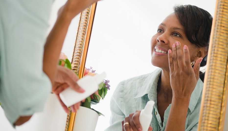 A woman applying moisturizer on her face in front of a mirror
