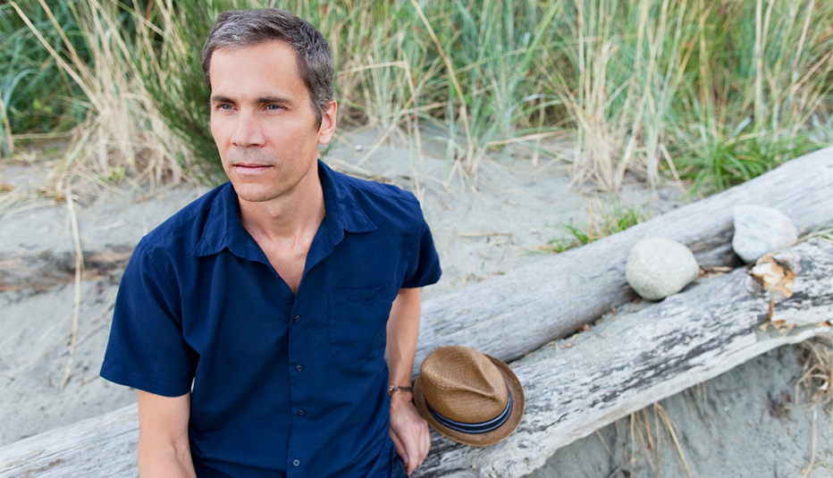 a mature man sits on driftwood and looks into the distance