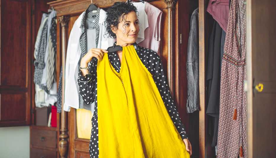 A woman is examining a yellow dress with her body in front of a mirror