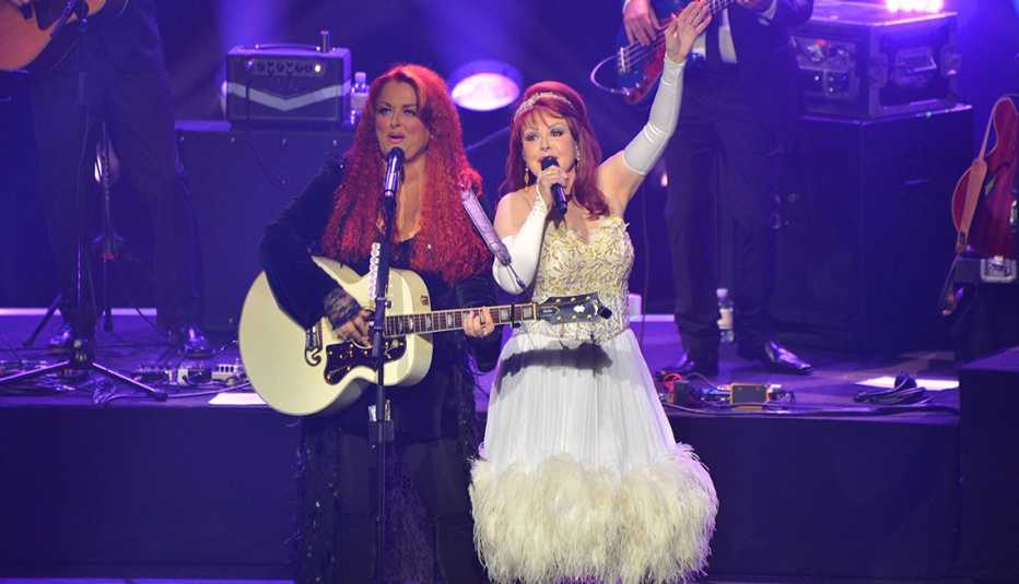 wynonna judd playing guitar and singing on stage with daughter naomi who is also singing