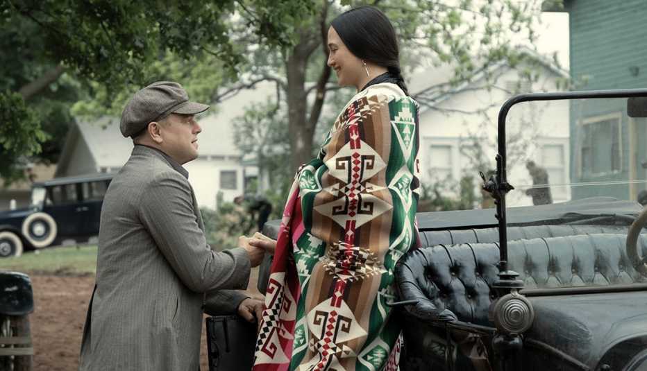 leonardo dicaprio helps lily gladstone get down from a vehicle in a scene from the film killers of the flower moon