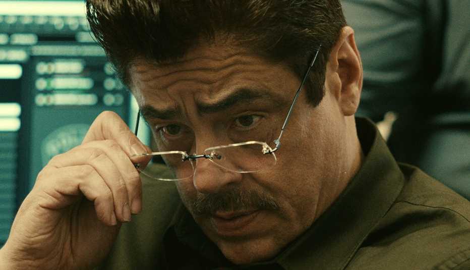 benicio del toro pulls down his glasses in a scene from the netflix film reptile
