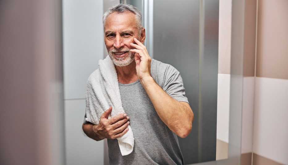 A man touches his face while looking at the bathroom mirror