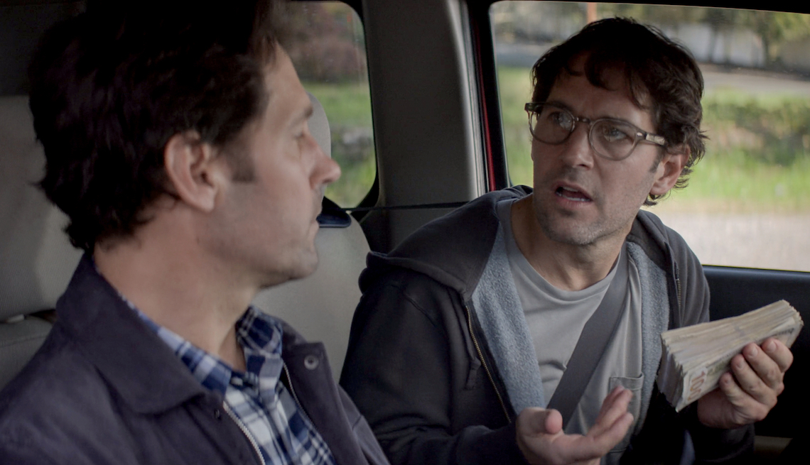 A scene inside a car, Paul Rudd holds money while talking to Paul Rudd in the limited Netflix series 'Living with Yourself'