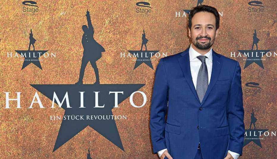 lin manuel miranda in front of a wall with the hamilton logo