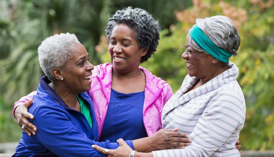 A group of three women standing together at the park, smiling, laughing and talking.