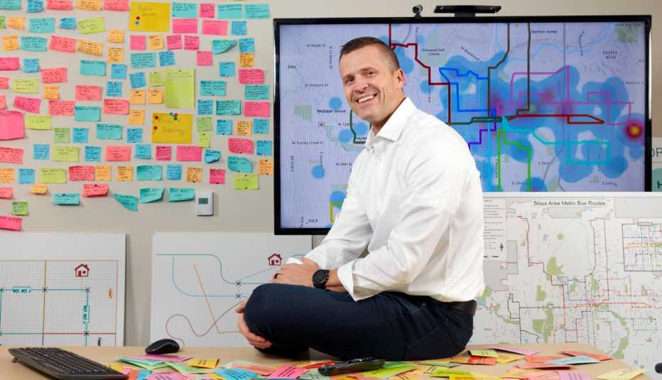 paul tenhaken the mayor of sioux falls south dakota sits on the desk in his planning office where the walls are covered in colorful post it notes and maps