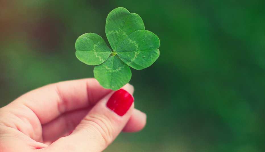 a hand with red nail polish holding a four leaf clover