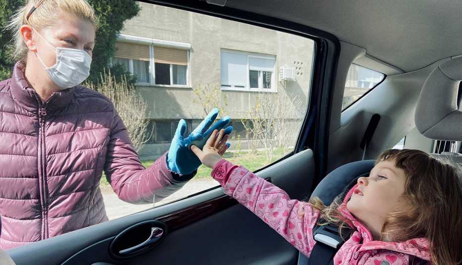 Woman touching her grandchild's hand through a car window, wearing a face mask