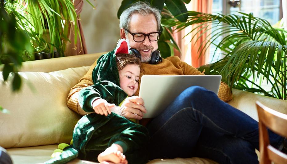 young girl cuddling with grandfather on sofa and playing online games together