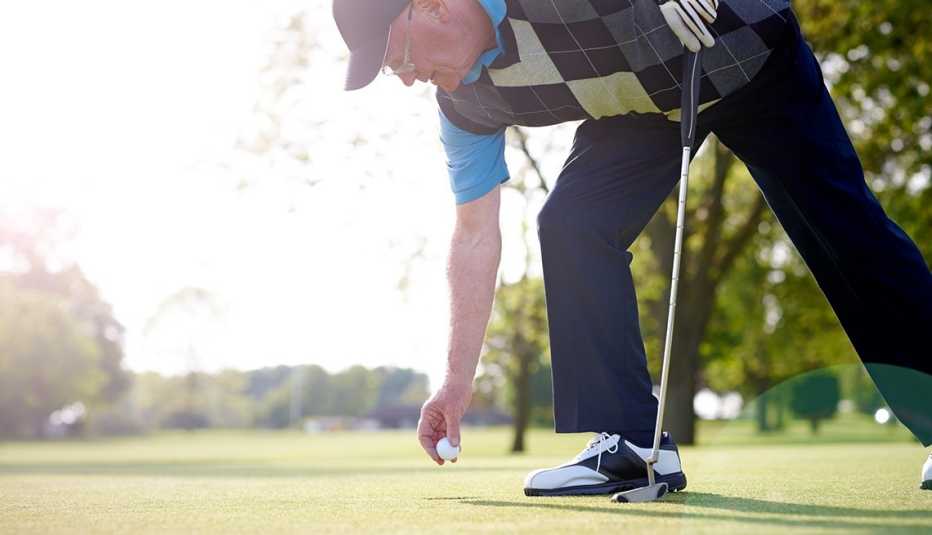 Senior male golfer taking ball out of the hole at golf course