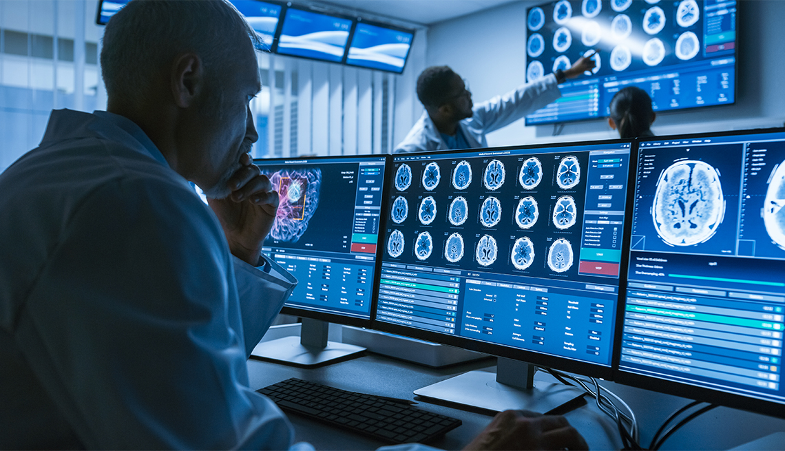 Over the Shoulder Shot of Senior Medical Scientist Working with CT Brain Scan Images on a computer