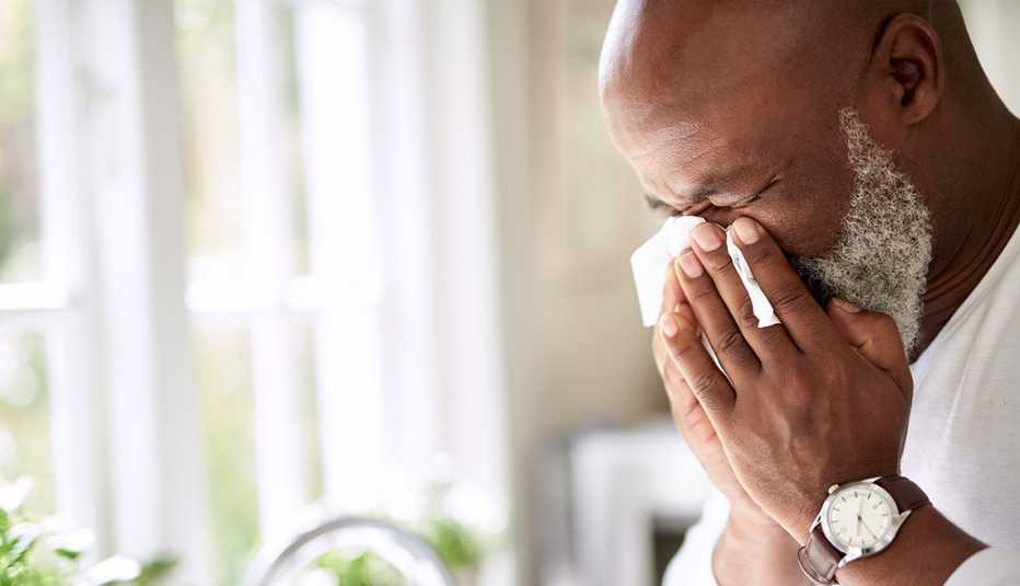 A man blowing his nose with a tissue at home