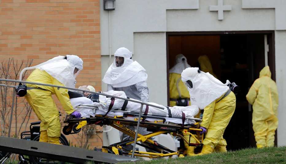 A man on a stretcher being moved from a nursing home by three people wearing medical protective gear
