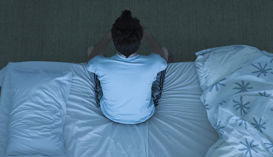 overhead view of a tired man sitting on the edge of his bed