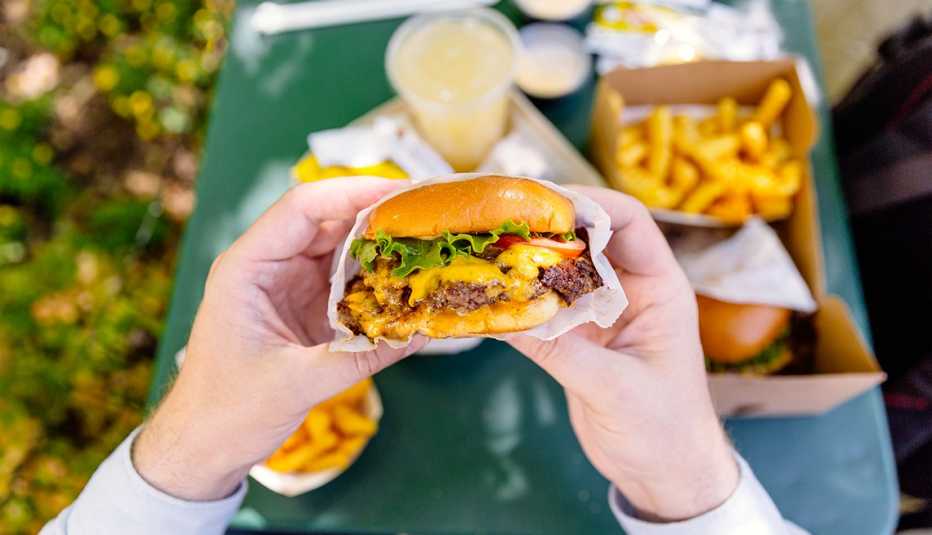 A personal perspective view of a man holding a cheeseburger over a table