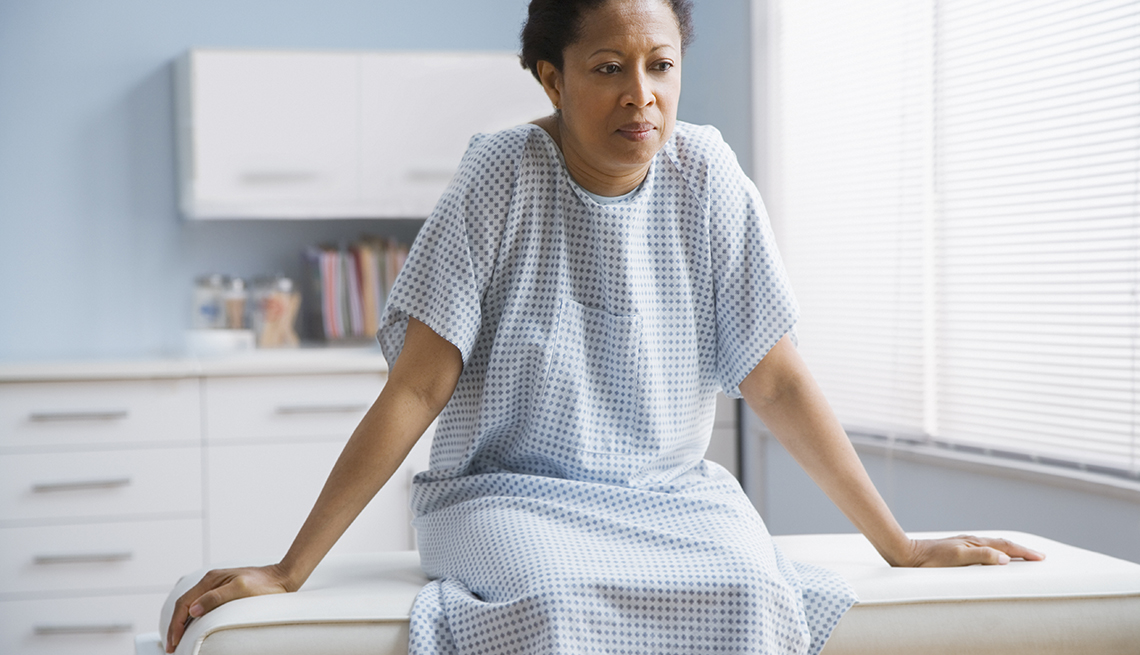 Mature African American woman sitting on the exam table in a doctor's office. She looks concerned.