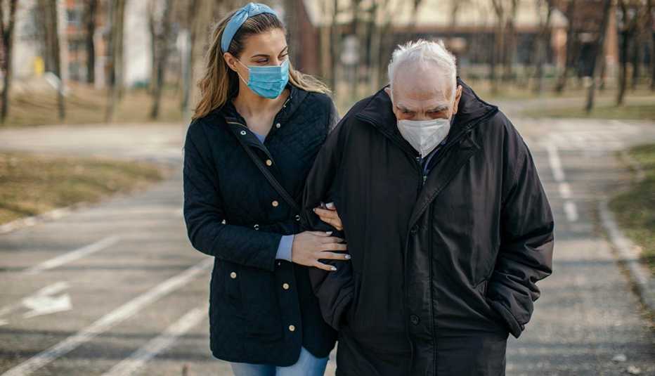 masked older man walking in park with masked caregiver by his side