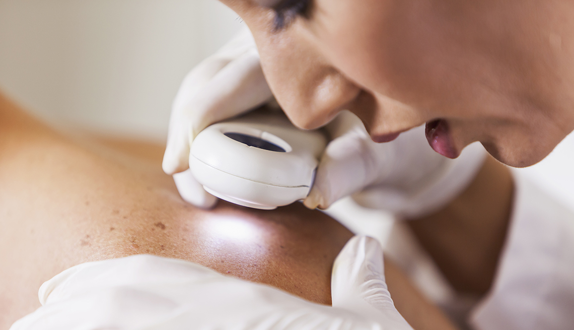 Female dermatologist examining patient's skin with dermascope for signs of skin cancer.