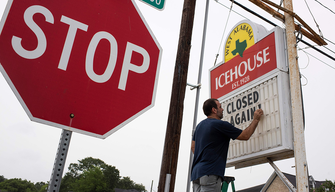 A man is putting a sign up outside of his bar that says it is closed again