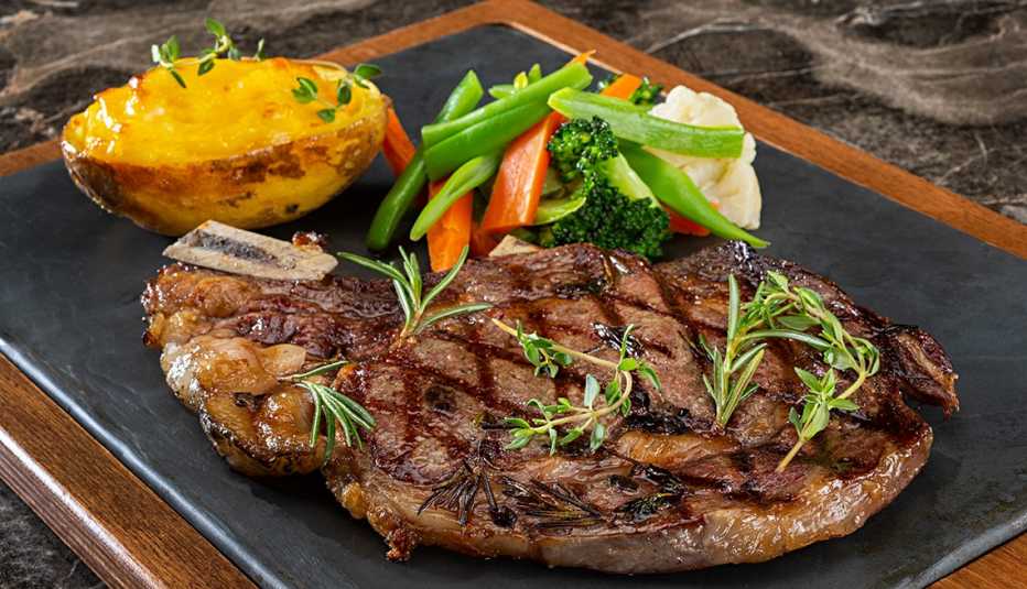 Close up of steak, vegetables and a baked potato on a platter.