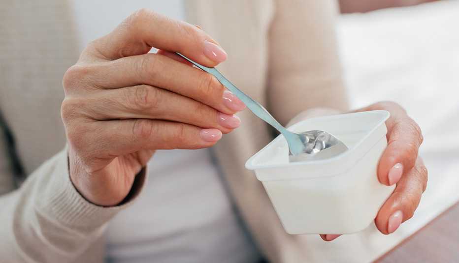 A close-up view of a woman using a spoon to eat yogurt from a white plastic container