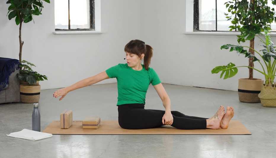 Side view of Erin Chiarelli sitting on mat with legs straight out in front, twisting to right with right arm extended back