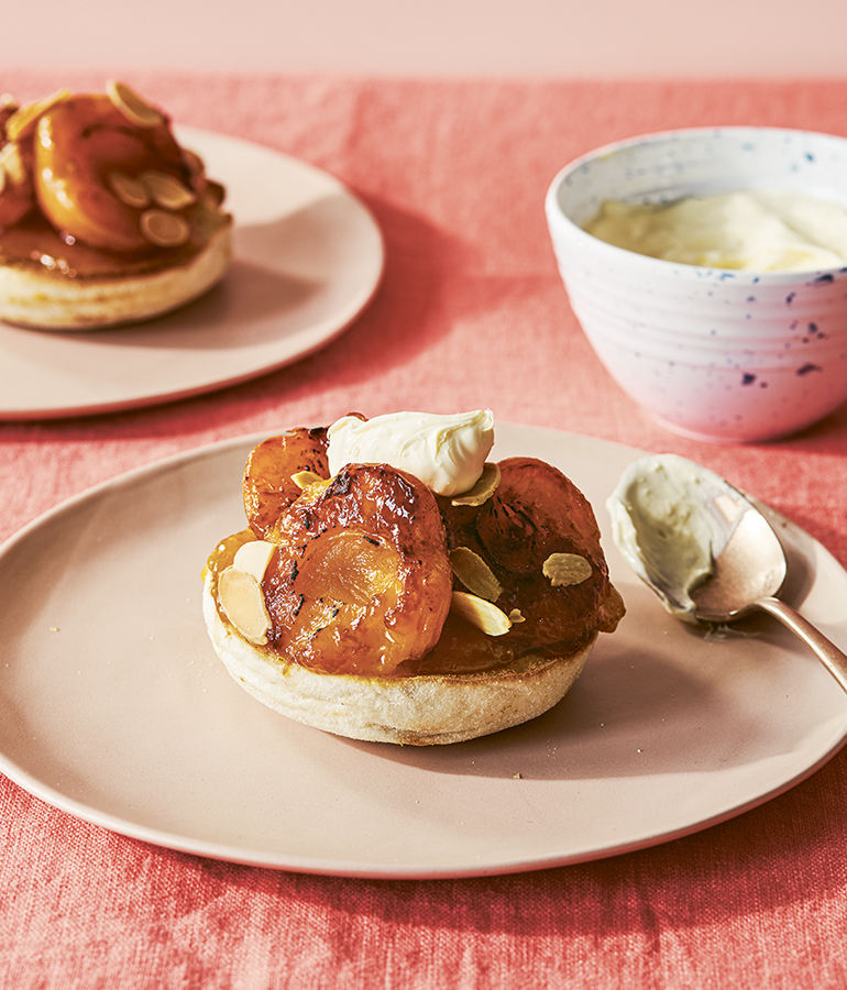 two english muffins with apricots, almonds and cream on plates; bowl of cream to right