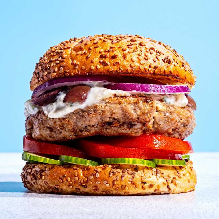 A hamburger with cucumber, tomato, red onion and sauce