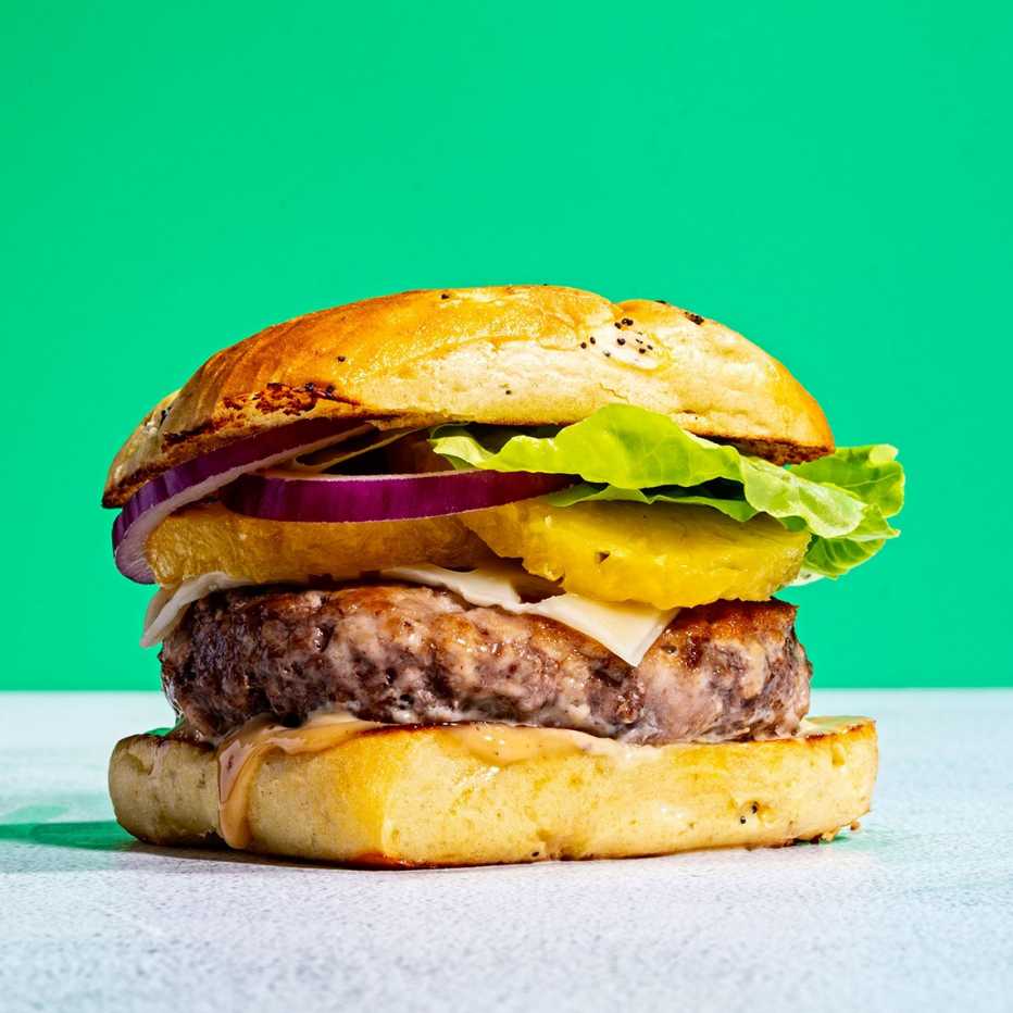 A hamburger with pineapple, onion, lettuce and sauce