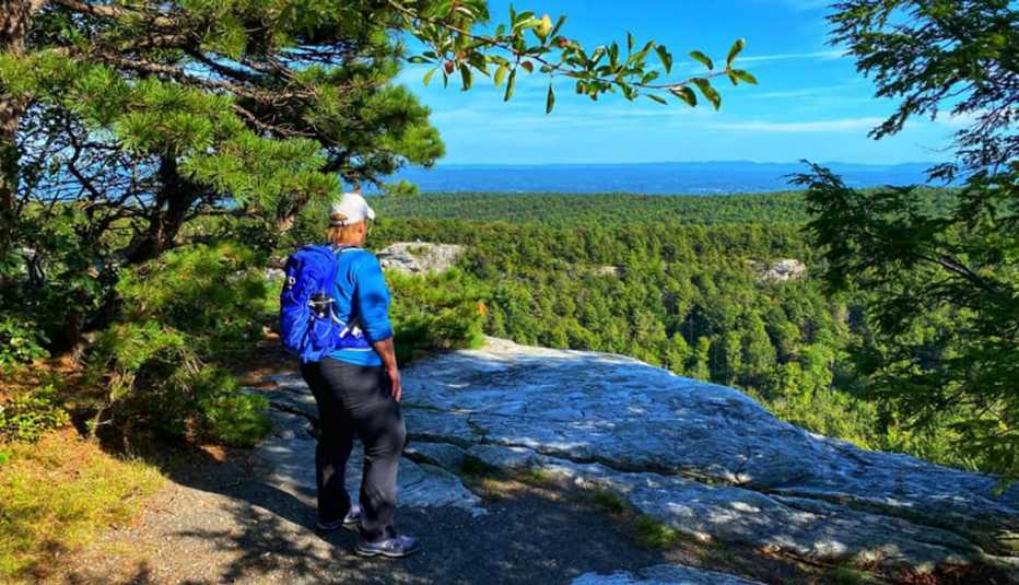 author Terri Marshall standing on a rocky ledge, looking out over the tops of green trees and distant mountains under blue skies