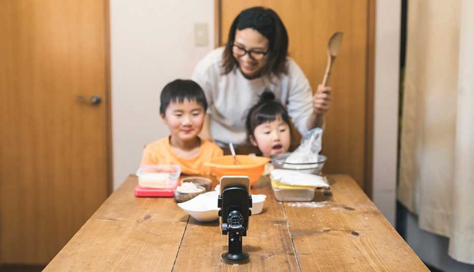 A mom and her two children baking holiday cookies with their grandmother using video chat on a mobile phone