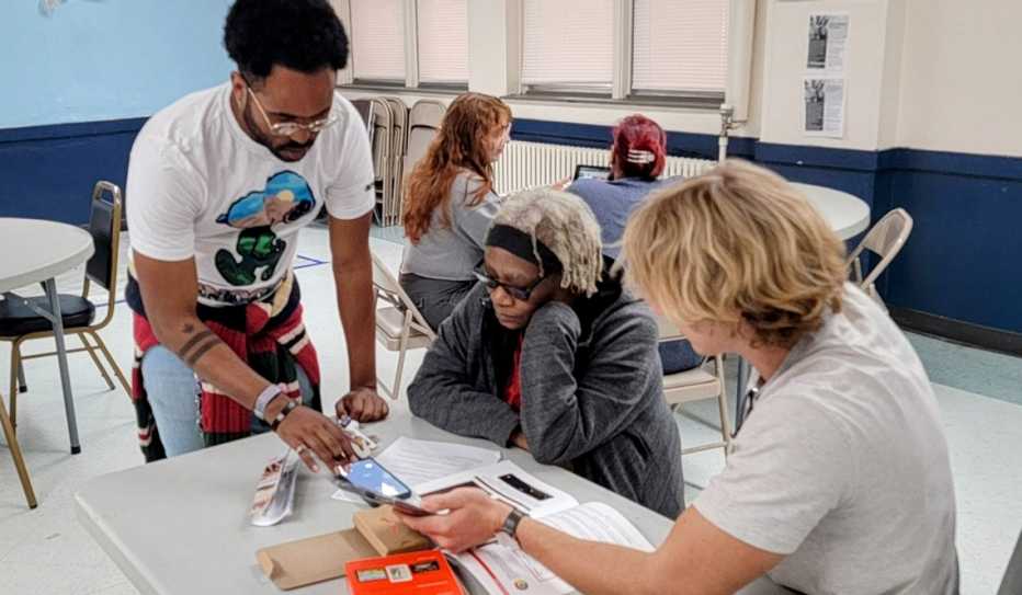 Two young men teach an older woman to use a smartphone