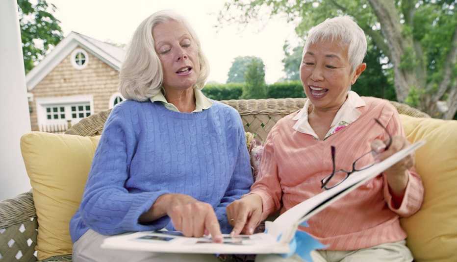 Two mature women looking at photo album on porch.