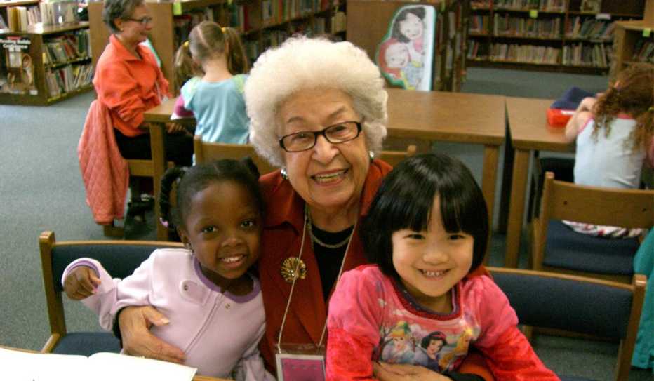 An older volunteer and two kindergartners smile during a Grandpals visit to the library