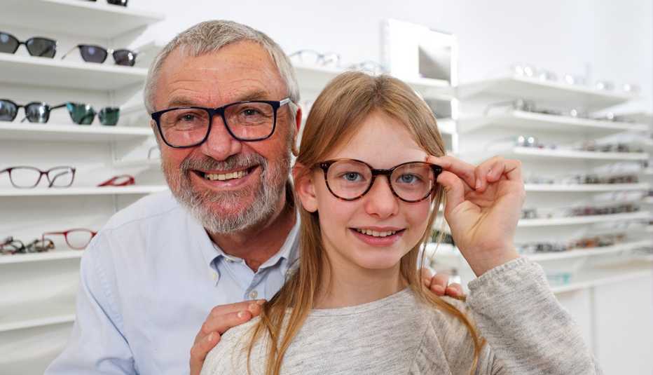 AARP member smiling with his grandaughter in a glasses shop while they both try on new frames
