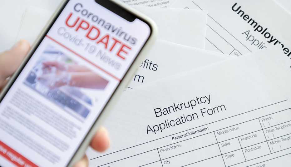 mobile phone with Coronavirus covid-19 news update. There is a bankruptcy and unemployment benefits application in the background on the desk