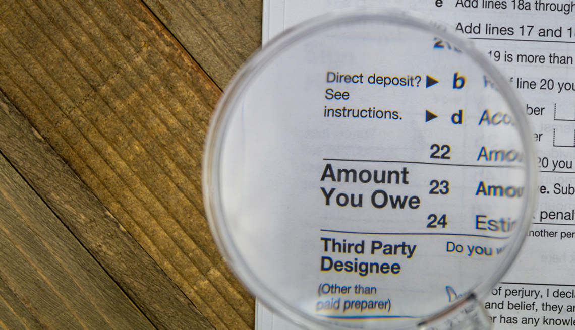 IRS tax Form on wooden surface with the "amount you owe" section under a magnifying glass