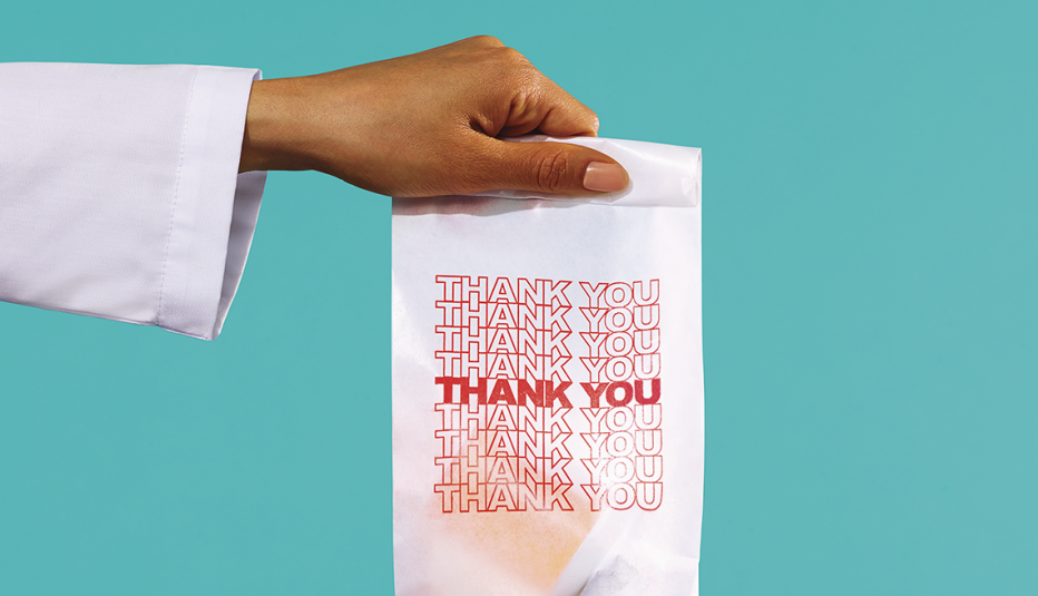 arm and hand of a pharmacist holding out a bag that contains a prescription medication